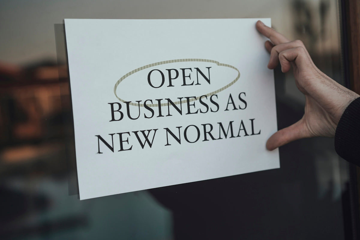 a person holding a sign that says open business as new normal