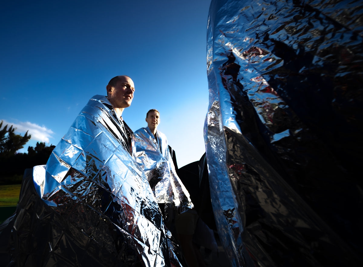 Two people wrapped in shiny emergency blankets outdoors.