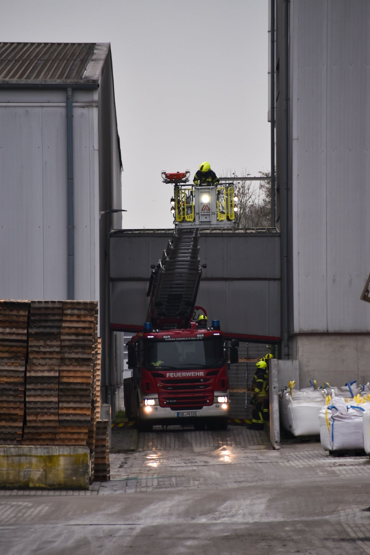 Firefighters operating a ladder truck at industrial building.