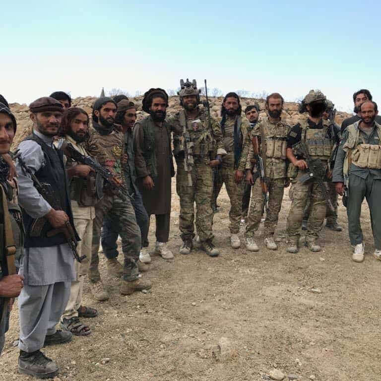 Group of armed men in military or paramilitary uniforms standing together outdoors.