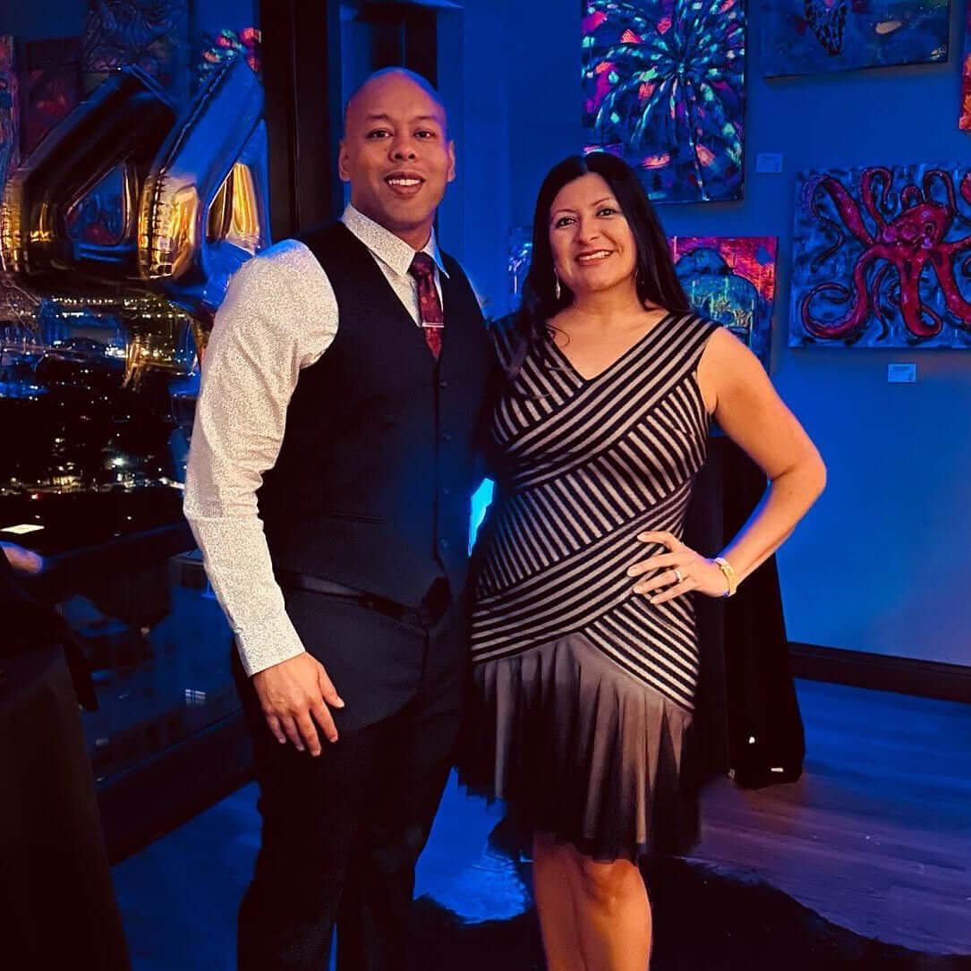 Man and woman posing together in a room with blue lighting and artistic wall decorations.