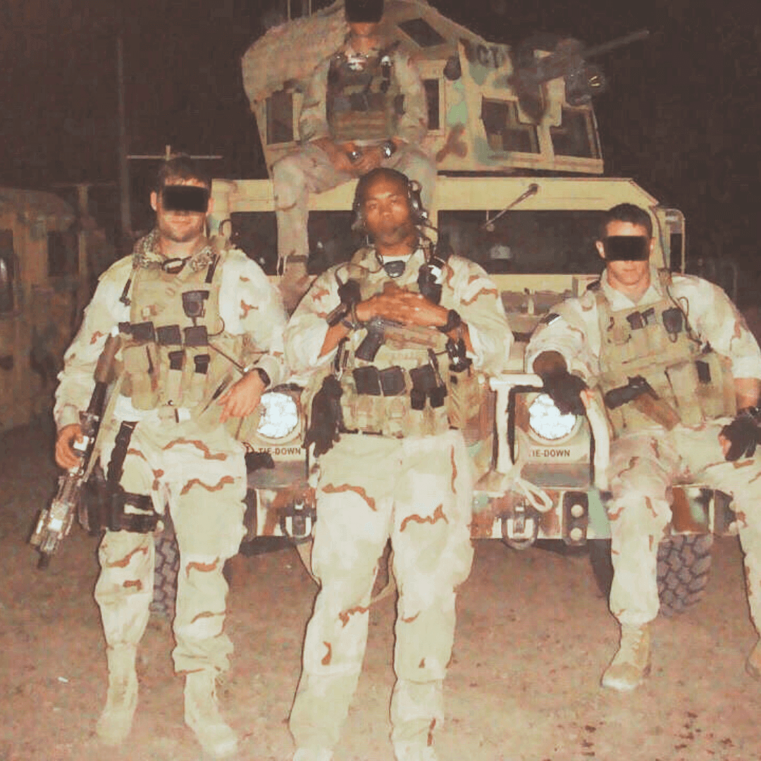 Three soldiers in camouflage uniforms standing in front of a military vehicle at night.